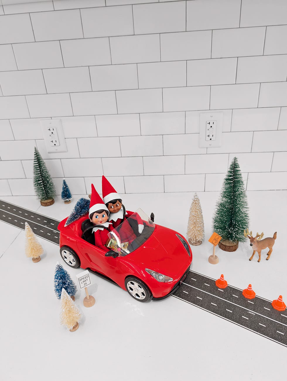 two elves in a hot toy car on a stretch of road with toy cones