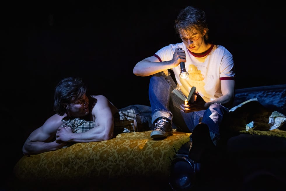 a couple of men sitting on a bed looking at a cell phone