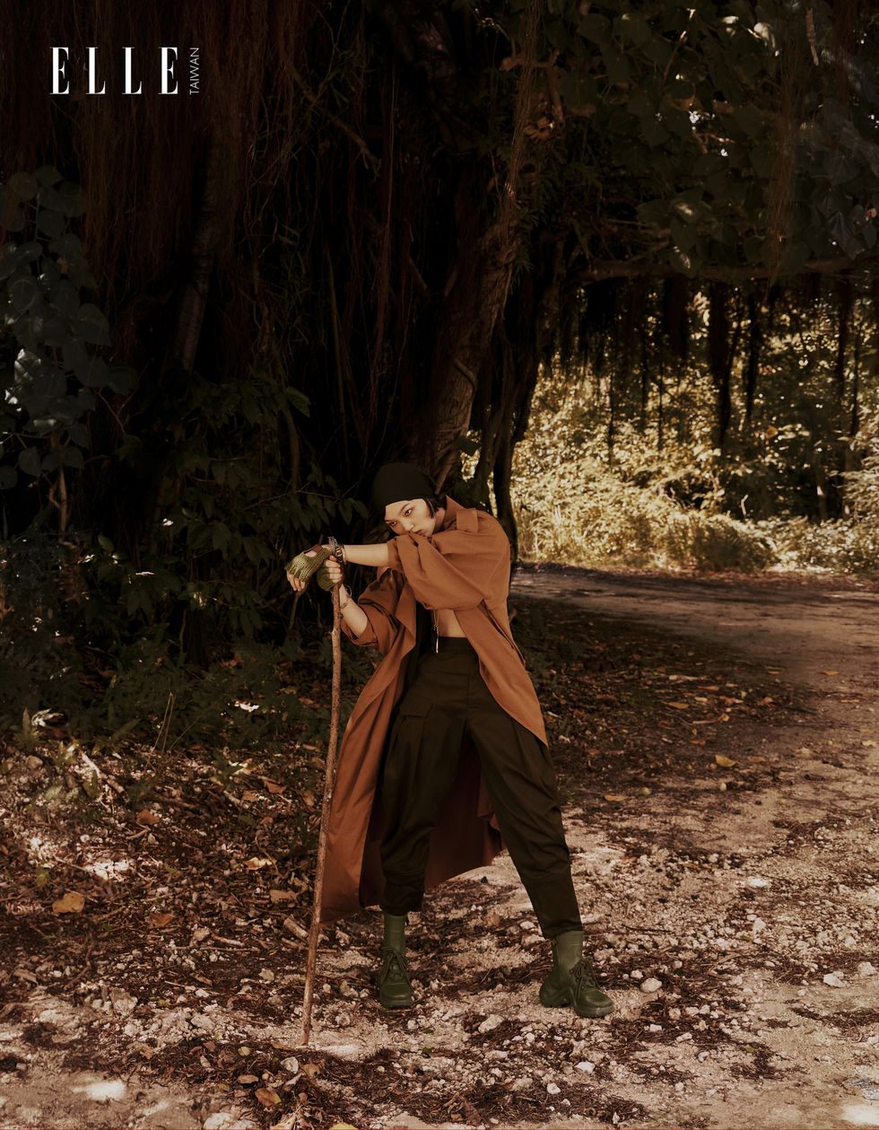一個女人穿著風衣拄著拐杖站在樹林裡