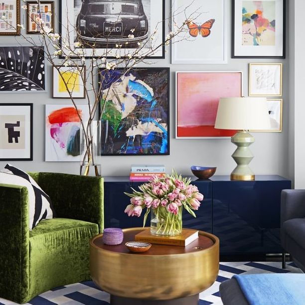 cozy living room with dark blue sideboard green velvet chair and round gilded table and blue and white rug and a back wall covered in framed prints and artwork