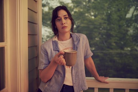 lizzy caplan holds a mug of coffee and stands on a deck in the fx miniseries 'fleishman is in trouble'