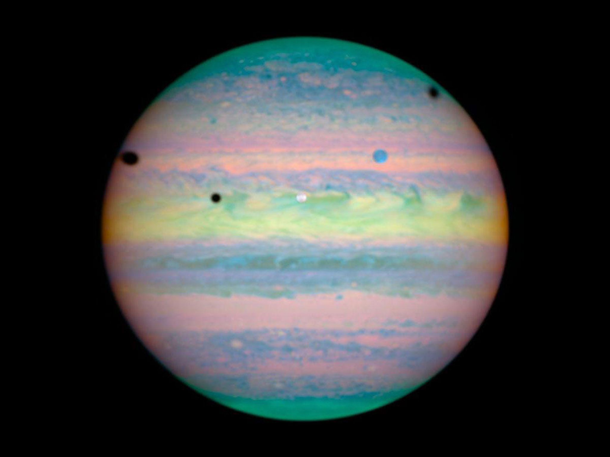 Op deze infraroodopname van de ruimtetelescoop Hubble doen de drie grote manen Io Ganymedes en Callisto zich voor als donkere vlekken tegen de achtergrond van Jupiters heldere wolkendek