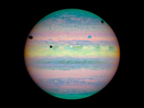 Op deze infraroodopname van de ruimtetelescoop Hubble doen de drie grote manen Io Ganymedes en Callisto zich voor als donkere vlekken tegen de achtergrond van Jupiters heldere wolkendek