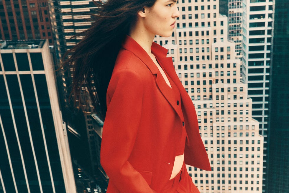 fashionable individual wearing a red suit against a cityscape background