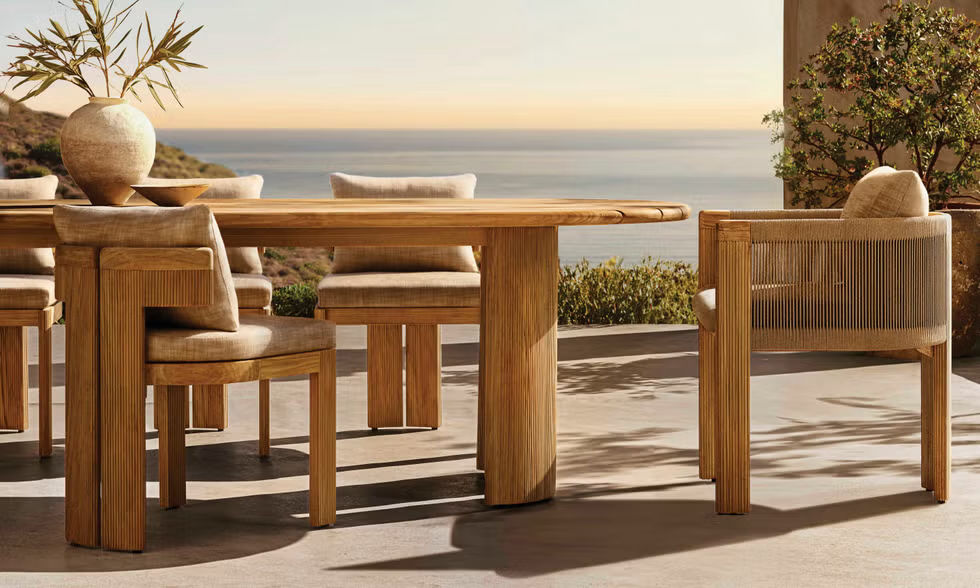 Outdoor dining setup with a wooden table and cushioned chairs overlooking a serene ocean view.