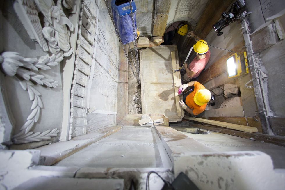 Werklieden maken een begin aan het verwijderen van de afgesleten marmerplaat die het oorspronkelijke graf eeuwenlang heeft afgedekt en leggen een laag van vulmateriaal eronder bloot