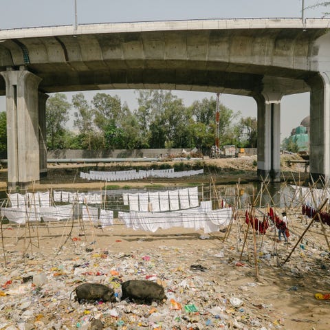 Pas gebleekte kleding hangt te drogen onder een viaduct in Delhi naast een open riool