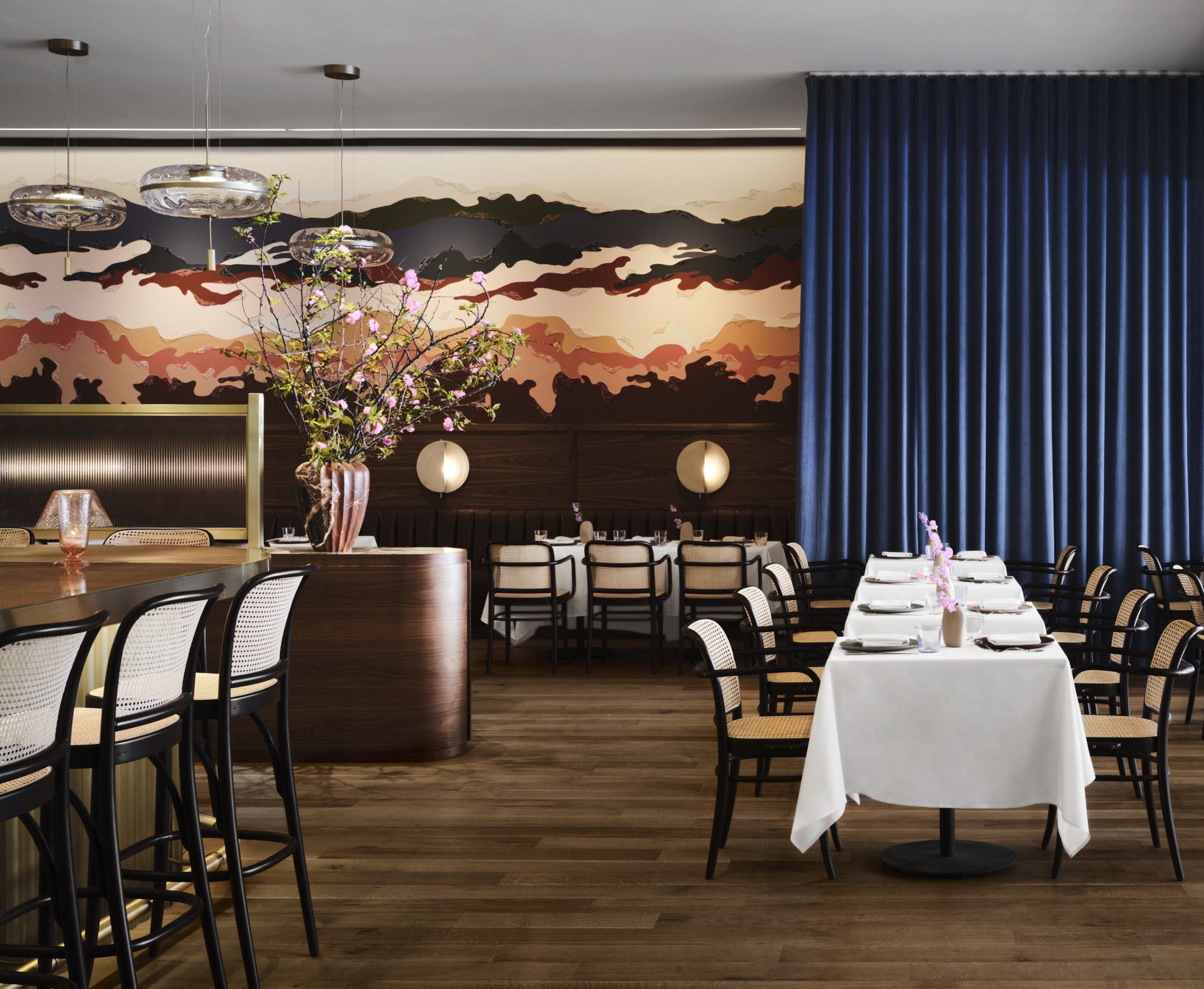 A List 2022 - ELLE DECOR interior of restaurant with bar stools on the left and matching table chairs and a painted all with wainscoting at the back