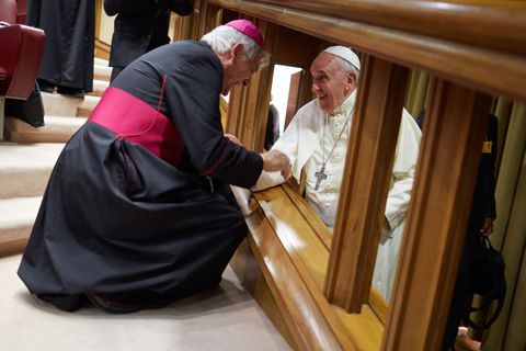Een bisschop knielt om de paus te begroeten als hij binnenloopt bij een bijeenkomst van bisschoppen en kardinalen om onderwerpen te bespreken over het gezinsleven zoals het huwelijk en scheidingen
