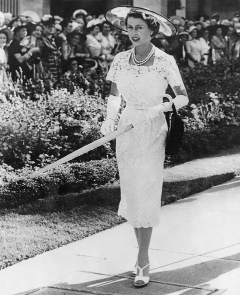 In een witte kanten jurk en met een strooien hoed flaneert Hare Majesteit naar een tuinfeest in Sydney tijdens haar eerste staatsbezoek aan Australi in februari 1954