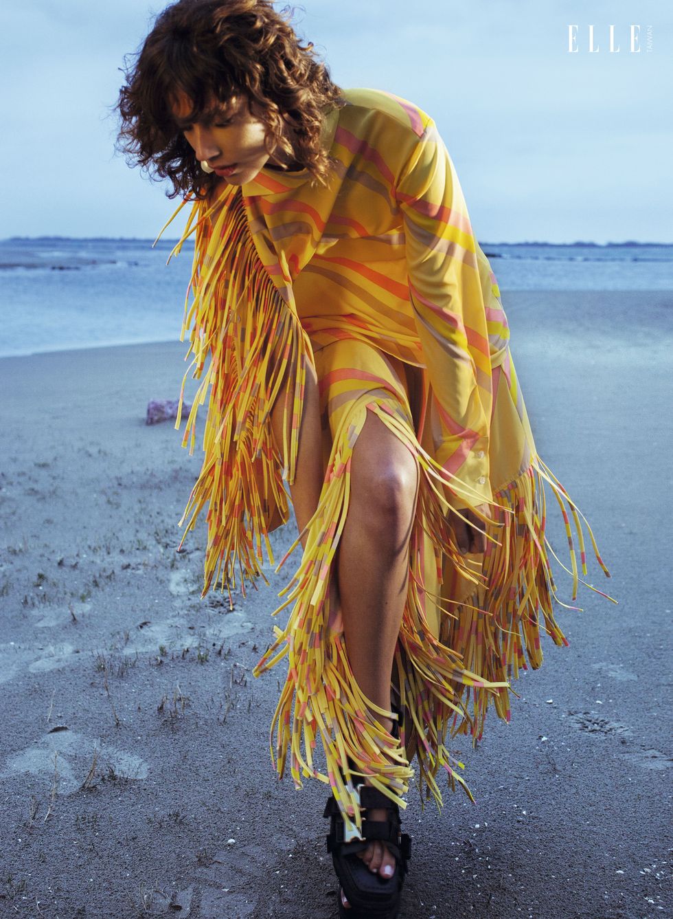 一個女人穿著流蘇洋裝站在沙灘中