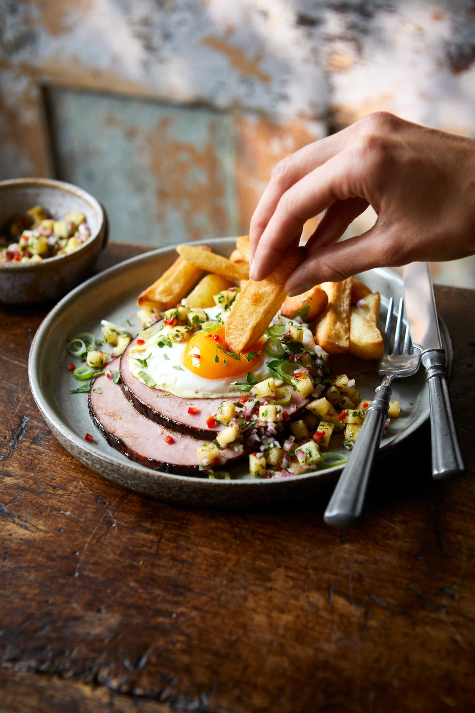a hand dipping a chip in to a fried egg with gammon
