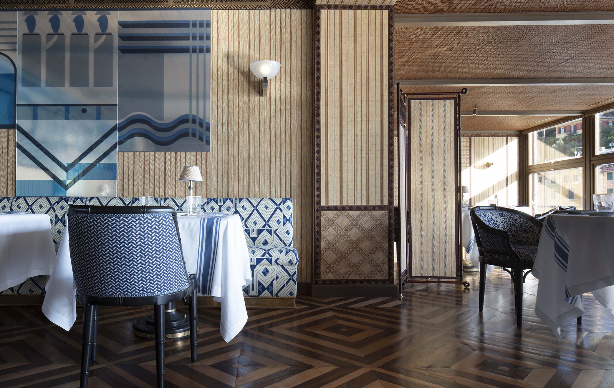 A List 2022 - ELLE DECOR interior of restaurant with blue trellis upholstered banquette and rattan looking chairs and a marquetry floor