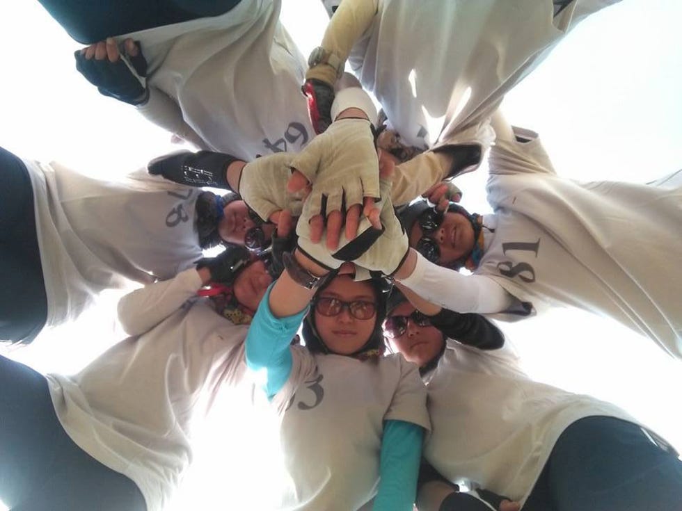 a circle of individuals dressed in matching shirts some wearing gloves with their hands reaching toward the center