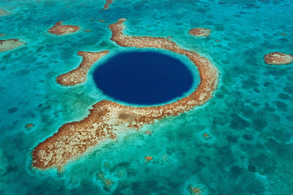 De Blue Hole in het Lighthouse Reef is een populaire toeristische attractie Een natuurlijk zinkgat zorgt voor het dramatische kleureffect