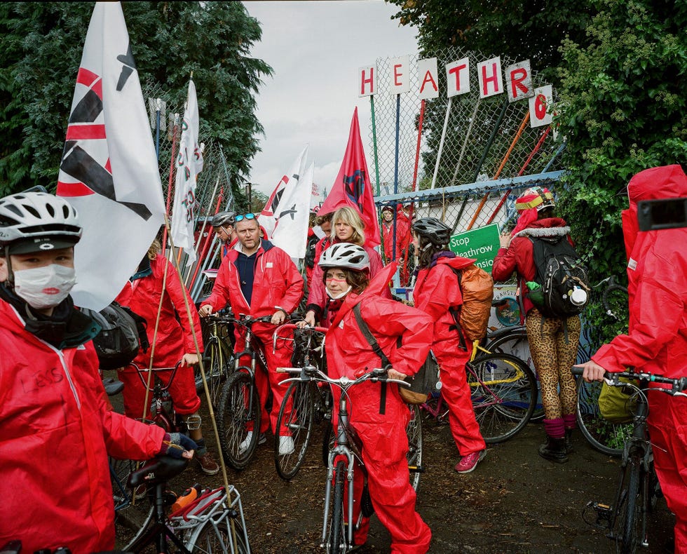 Fietsers in felgekleurde pakken rijden langs de omheining van de luchthaven Heathrow om aandacht te vragen voor de uitbreidingsplannen Grow Heathrow begon als een protestkamp tegen de aanleg van een derde startbaan Bewoners en activisten hopen nog altijd dat ze de uitbreiding kunnen tegenhouden