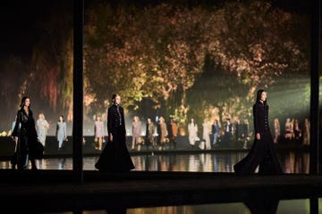 Fashion models walk along a runway surrounded by a serene outdoor setting