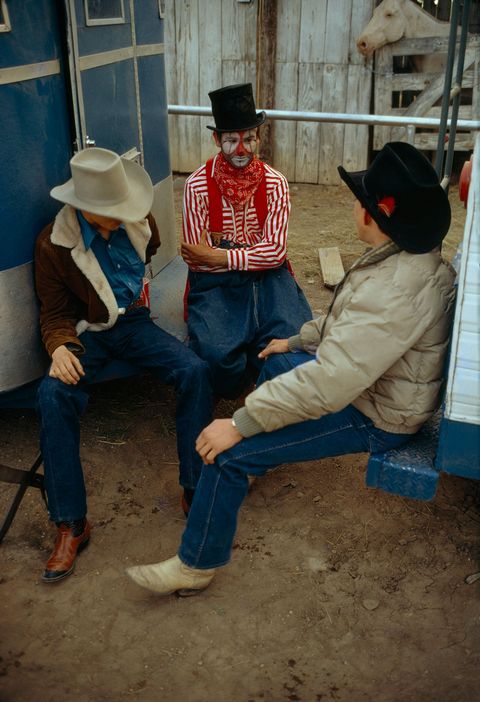 Een rodeoclown zit tussen twee als cowboy geklede mannen in Wyoming in de vroege jaren 1970 Rodeoclowns dienen tussendoor als entertainment bij stierenberijdshows in de Verenigde Staten