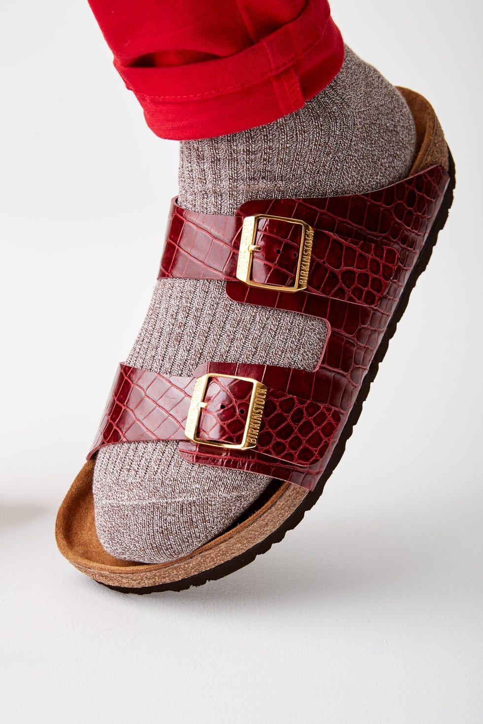 cropped view of a foot wearing a burgundy buckle sandal with textured socks