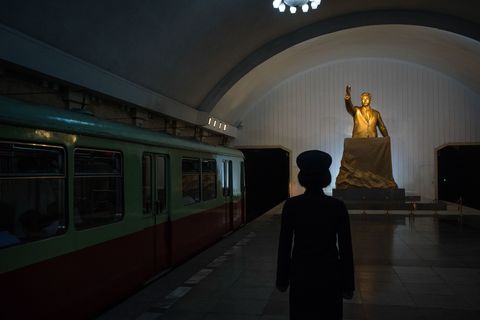 Een conducteur staat voor een beeld van Kim Ilsung in een metrostation in Pyongyang