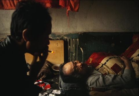 In het industrile district Tiexi in China rookt een man een sigaretje naast zijn bedlegerige en slapende vader