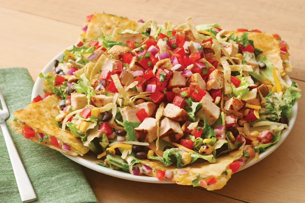 a large salad featuring greens grilled chicken and various toppings served on tortilla chips