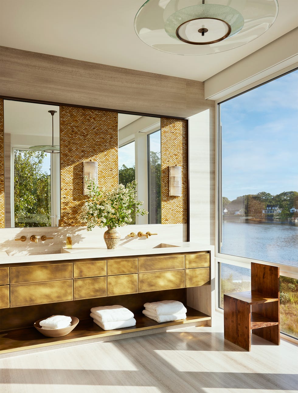 Modern bathroom with a view of water, featuring a luxurious vanity, decorative flowers, and natural light.