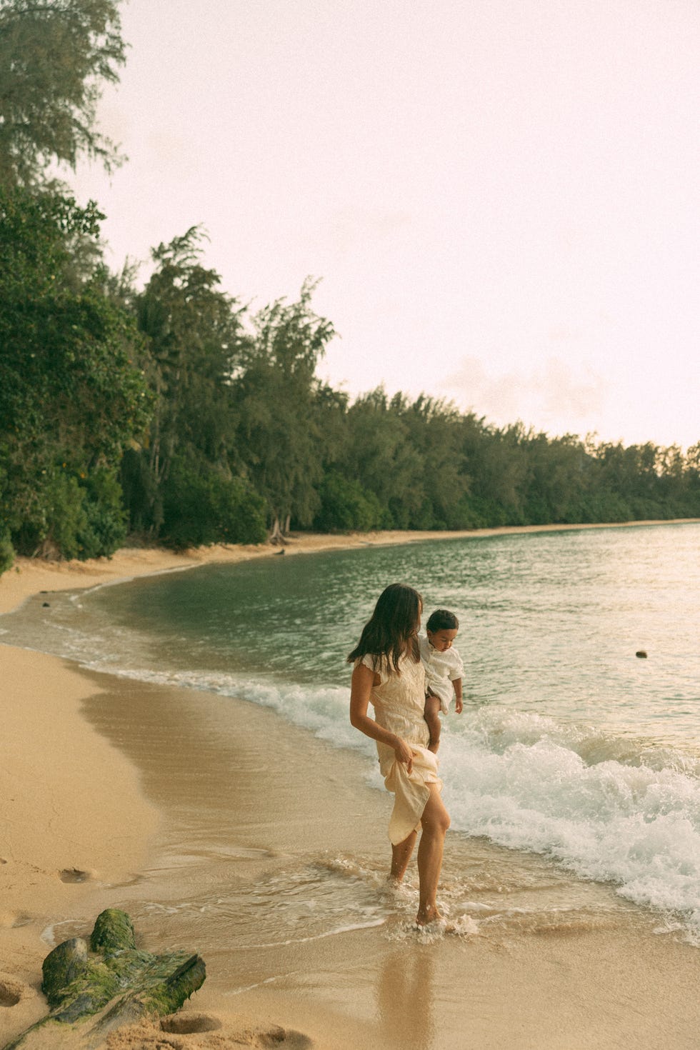a woman walking along a beach shoreline while holding a child