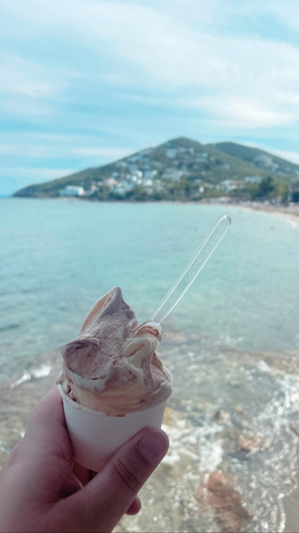 a hand holding a cup of ice cream with a spoon