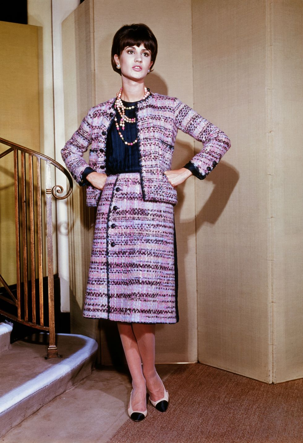 original caption paris wrap around chic following her typical silhouette, good chanel creates this suit for fall 1963 with a colorful flair the illustrious paris designer selects a colorful combination of pink, mauve, and navy blue tweed for the suit and binds the casually chic jacket in the contrasting navy the skirt is slender and wraps around the figure with a four buttoned closing at one side
