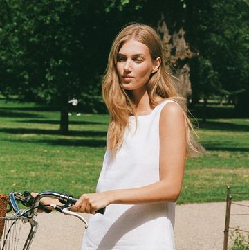 a woman in a white linen dress by posse standing next to a bicycle