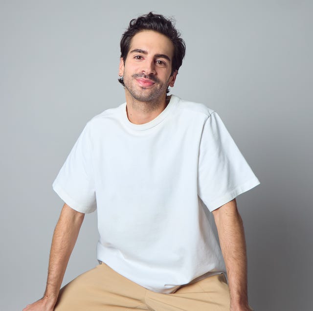 a person sitting in a white shortsleeve shirt and beige pants against a gray background a person sitting in a white shortsleeve shirt and beige pants against a gray background