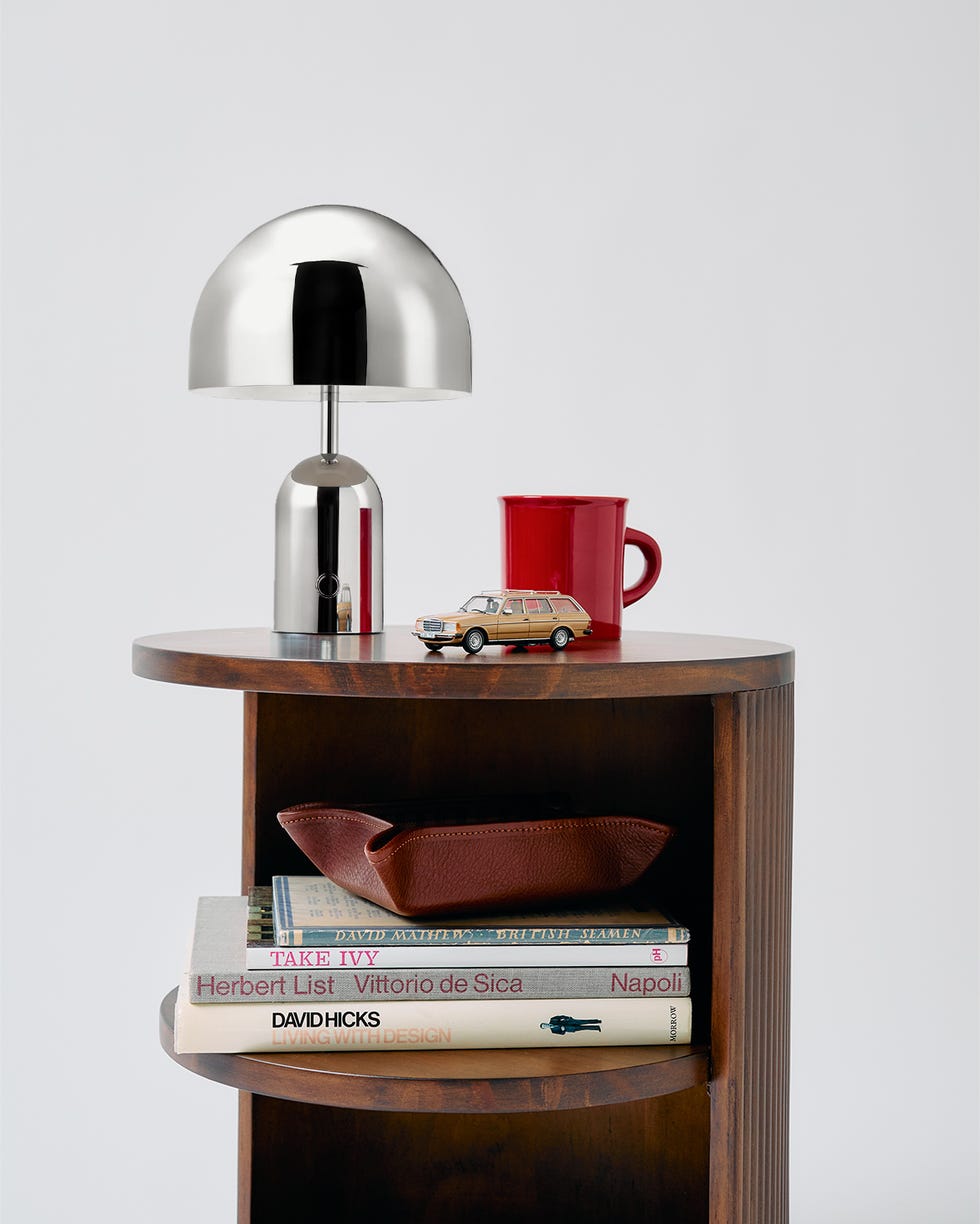 a modern table lamp placed on a wooden shelf alongside books and decorative items