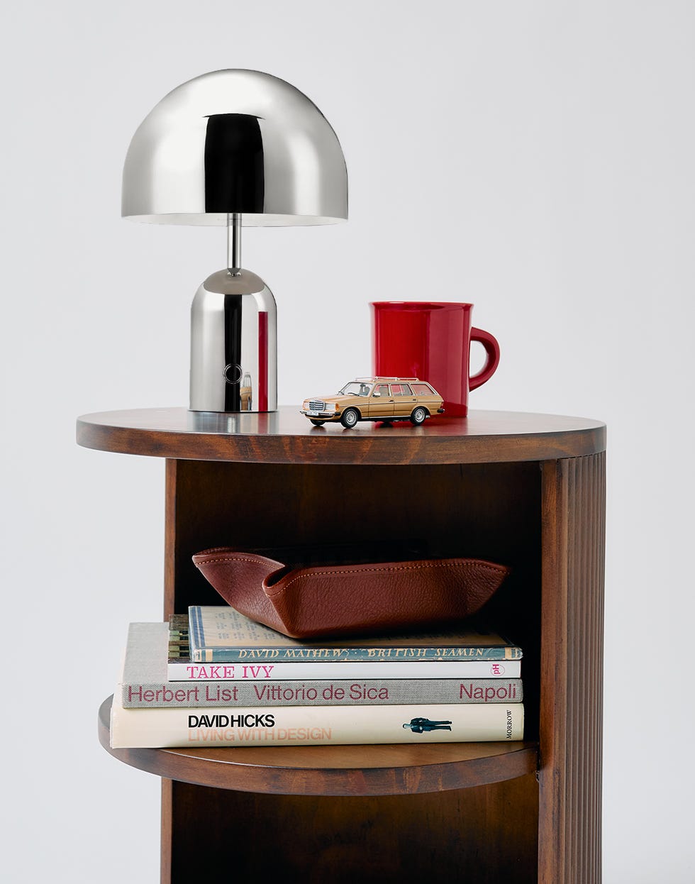 a modern table lamp placed on a wooden shelf alongside books and decorative items