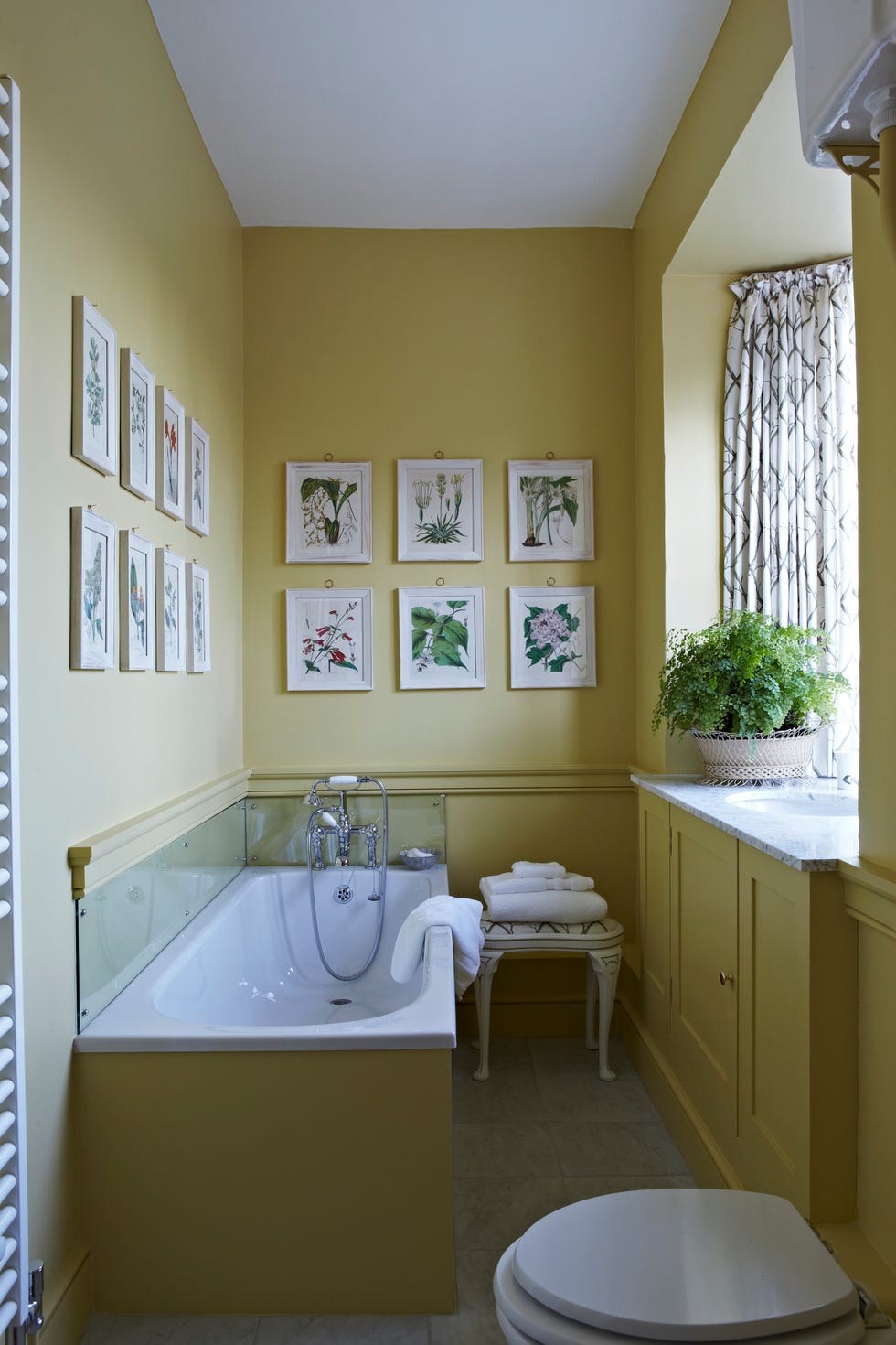 a yellow green bathroom with tub and botanical prints