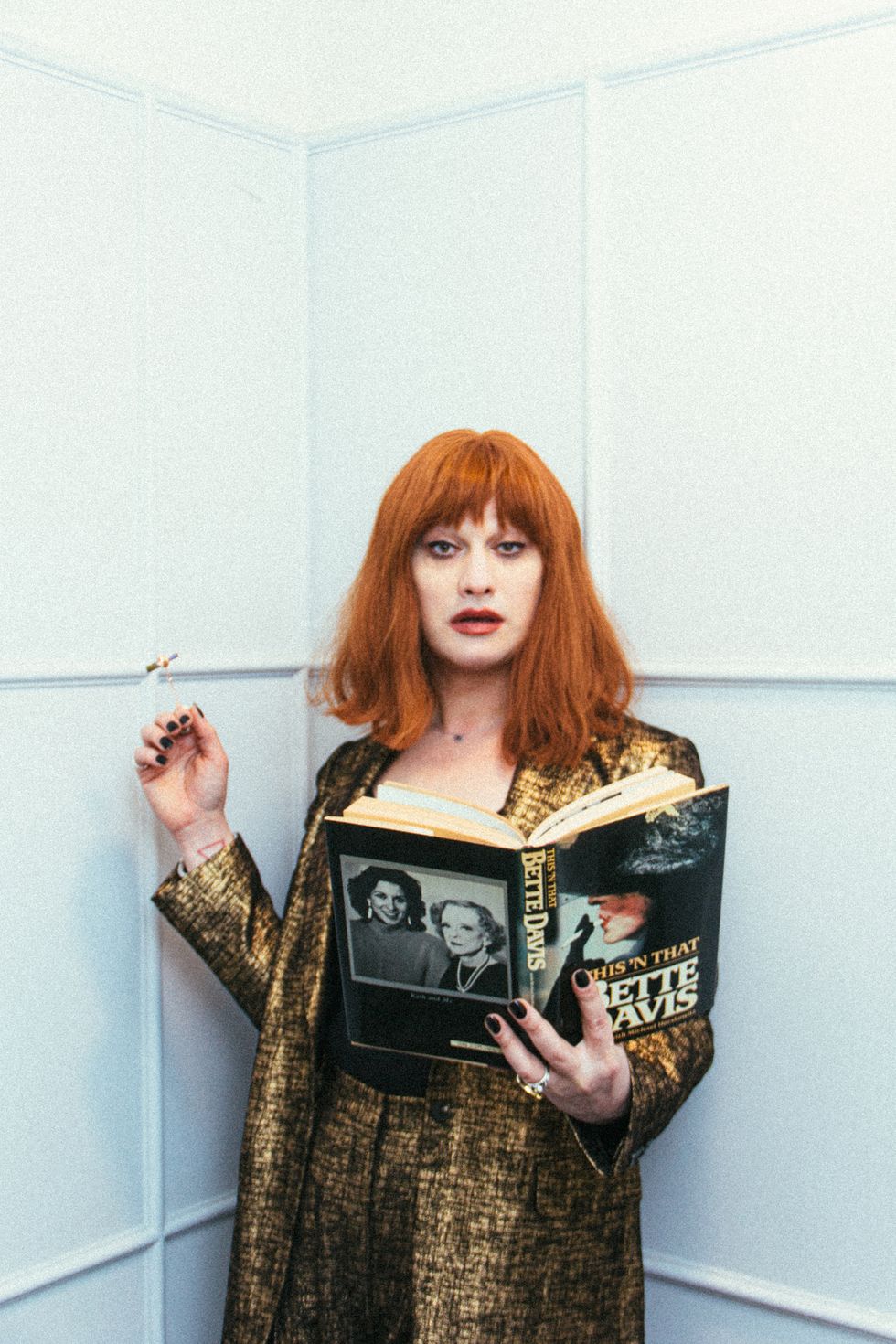 jinkx monsoon posing in gold with a bette davis book