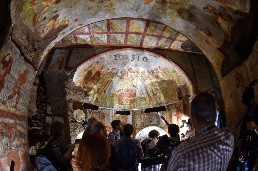 Bezoekers bewonderen een gerestaureerd fresco in de catacomben van Domitilla
