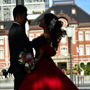 東京駅を背景に向き合って立つ赤いドレスの花嫁とタキシード姿の花婿