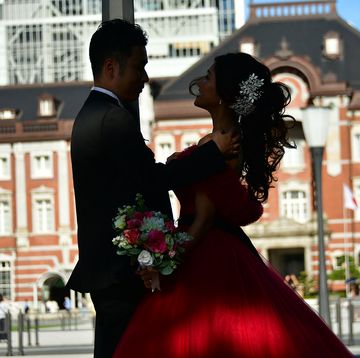 東京駅を背景に向き合って立つ赤いドレスの花嫁とタキシード姿の花婿