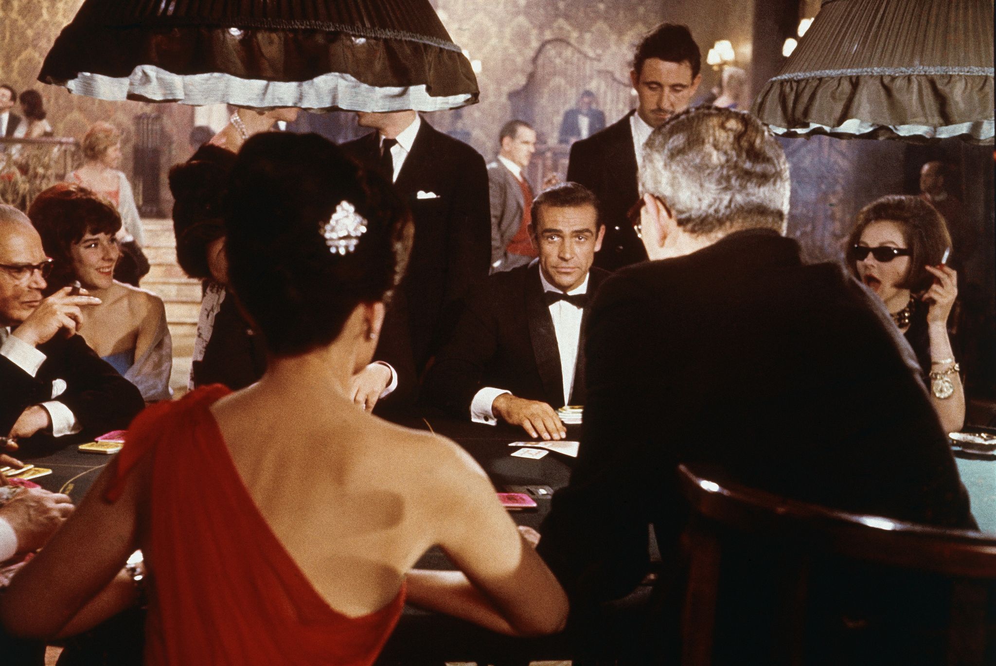 scottish actor sean connery center as fictional secret agent james bond sits at a casino card table in a scene from the film dr no, directed by terence young, 1962 british actress eunice gayson sits with her back to the camera in a red, off the shoulder dress photo by mgm studioscourtesy of getty images