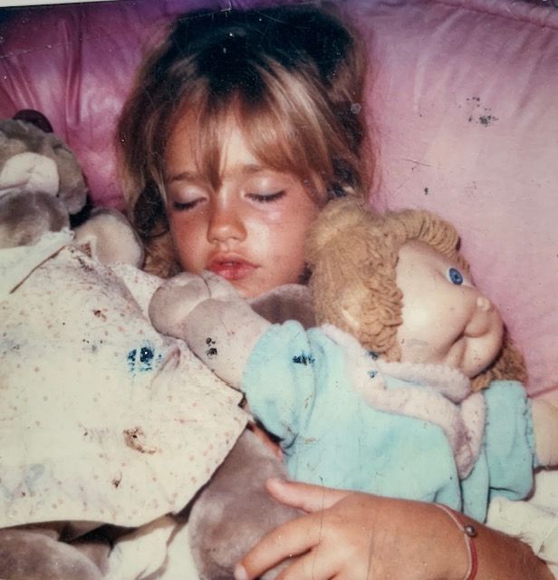 a toddler photo of actress minka kelly asleep, clutching her cabbage patch doll