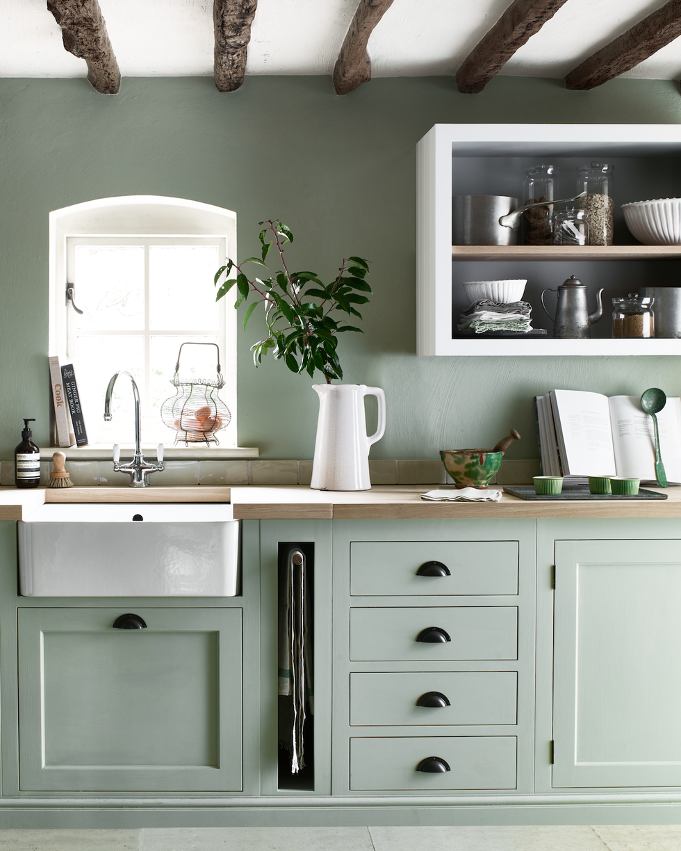 a sage green kitchen in a country cottage with built in storage and a butlers sink