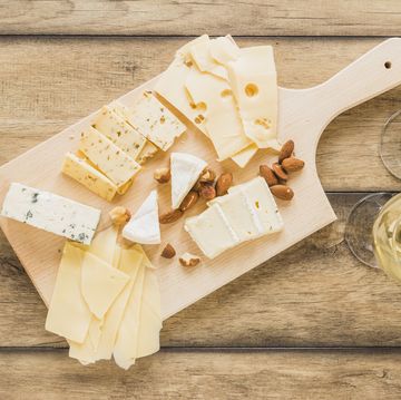 cheese board with various cheeses placed on wooden counter top with wine and bowl of nuts