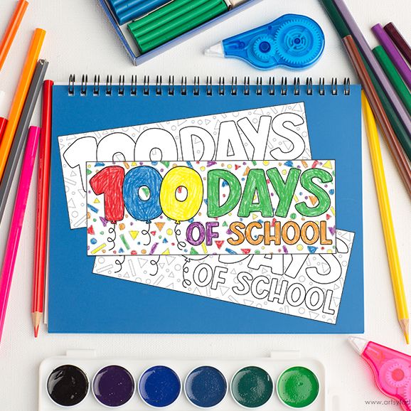 a 100 days of school bookmark sits on a desk with a notebook and school supplies