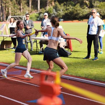 woman runner hands baton to other runner on track
