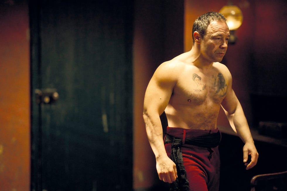 a muscular man in a dimly lit room wearing red pants