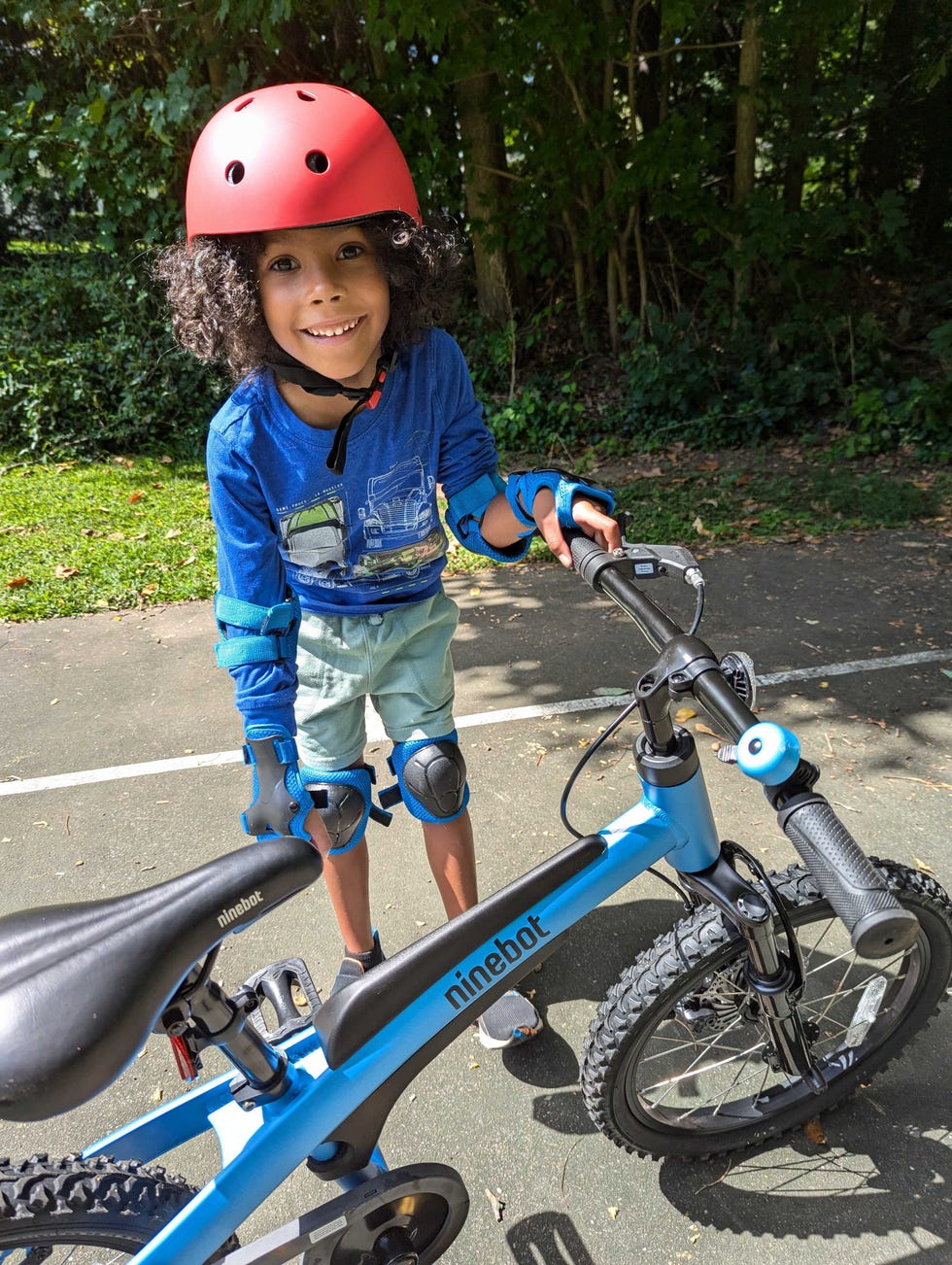 a child wearing safety gear stands next to a blue bicycle, testing for the good housekeeping institute