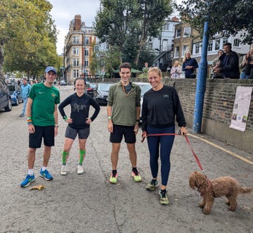 four individuals in casual athletic clothing with a dog standing on a street