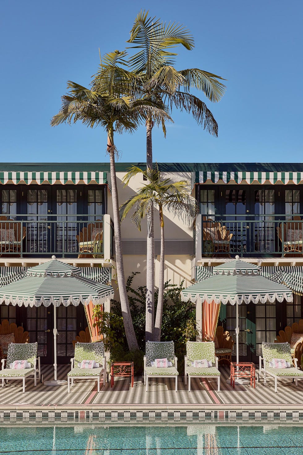 A poolside view of a sunlit courtyard featuring tropical plants and lounge chairs.