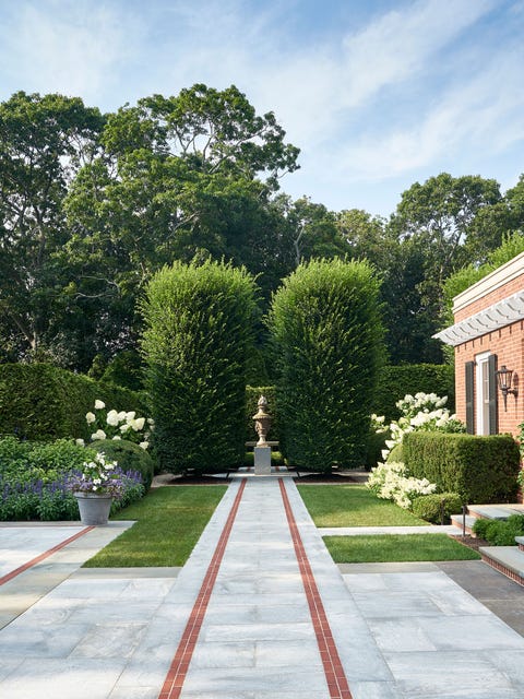 Classic long paved walkway to a pedestal with an urn between two large pine trees